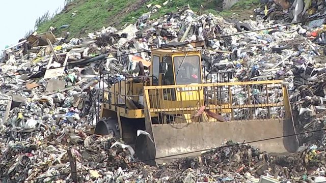 huge tractor with a front end loader and metal wheels is used to move trash in a city dump. 