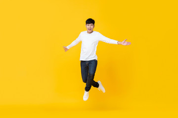 Fototapeta na wymiar Excited asian man jumping over yellow background