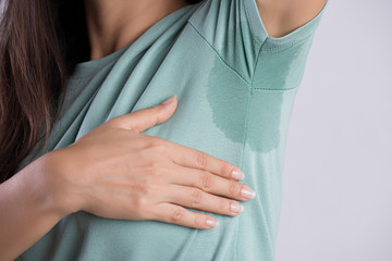 Close-up asian woman with hyperhidrosis sweating. Young asia woman with sweat stain on her clothes against grey background. Healthcare concept. - obrazy, fototapety, plakaty