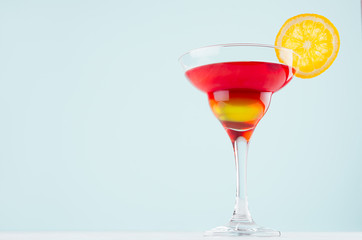 Alcohol cocktail for celebration  with red and yellow liquor, orange slice in mint color bar interior on white wood table.
