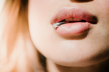 A young girl holds a ring in her lips. A ring in a woman's mouth