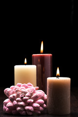 Three lit candles on wooden table with black background and a pink flower arrangment. Rembrandt lighting inspired Christmas scene.