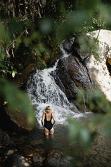 young slim girl in the jungle stands in the water in front of a waterfall