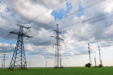 High-voltage power lines passing through a green field, on the background of a beautiful cloudy sky