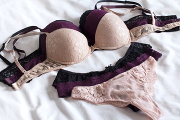 black beige and purple sets of women's underwear on a bed with white sheet