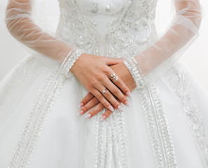 Bride is holding hands with golden rings on her luxury long sleeve dress. Beautiful nails. Artificial crystal diamonds. Wedding jewellery.