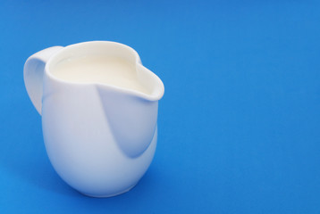 Fresh milk in white jug on blue background with copyspace