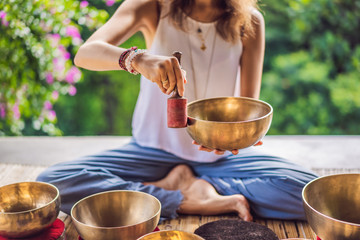 Woman playing on Tibetan singing bowl while sitting on yoga mat against a waterfall. Vintage...