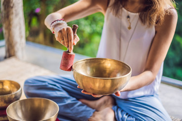 Woman playing on Tibetan singing bowl while sitting on yoga mat against a waterfall. Vintage...