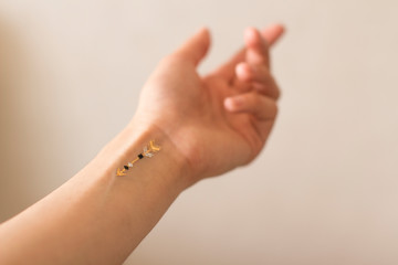 young woman's hand with gold arrow tattoo on her wrist on white background