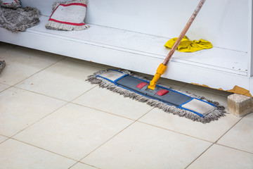 Wooden mop with large pile for washing floors on tile.