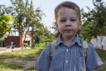 a beautiful little boy in the yard with a backpack