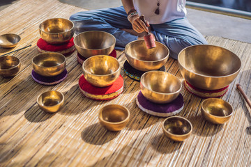 Woman playing on Tibetan singing bowl while sitting on yoga mat against a waterfall. Vintage tonned. Beautiful girl with mala beads meditating