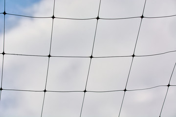 Wicker volleyball net against the blue sky with clouds.