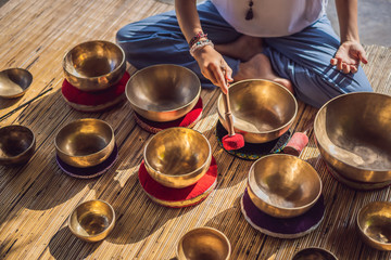 Woman playing on Tibetan singing bowl while sitting on yoga mat against a waterfall. Vintage tonned. Beautiful girl with mala beads meditating