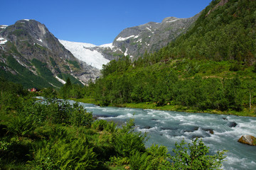 Fototapeta na wymiar Travel to Norway, the blue mountain river flows among stones and bushes from a high mountain with a glacier