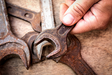 Old and rusty wrench in hand on wooden background.  Construction and hand tools, maintenance and reparing concept