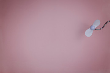 Small white plastic fan on a pink background. Place for text