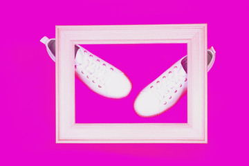 White sneakers are lying on neon pink background. Top view. Flat lay. Copy space.