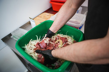 Cooking skewers of pork, mixing pieces of meat with marinade, onions. Hands in gloves in a green bowl marinate meat for barbecue for sale