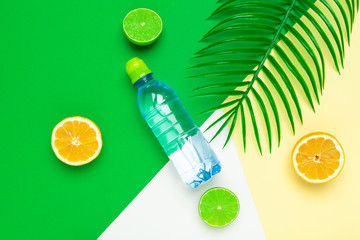Tropic leaves and bottle l water on yellow background. Detox fruit infused water.