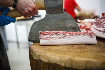 The process of cutting and chopping meat. A man in gloves with an axe and a saw cuts the meat on a special wooden table, pieces of raw meat hanging on hooks