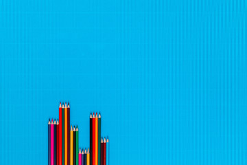 A bunch of crayons on a blue background, shot from above, aligned at the bottom left.