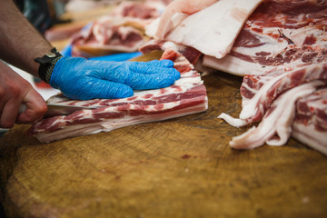 Fototapeta premium The process of cutting and chopping meat. A man in gloves with an axe and a saw cuts the meat on a special wooden table, pieces of raw meat hanging on hooks