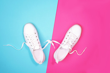 White sneakers are lying on bright neon color blue pink background. Top view. Flat lay. Copy space.