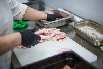 The process of preparing meat products. Gloved hands are molded from ground beef and bacon patties
