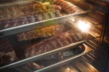 Smoked meat products in the oven smokehouse. A man holding a tray of smoked meat products
