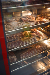 Smoked meat products in the oven smokehouse. A man holding a tray of smoked meat products