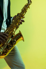 Young african-american jazz musician playing the saxophone on gradient yellow-green studio background. Concept of music, hobby, festival. Joyful attractive guy improvising. Colorful portrait of artist