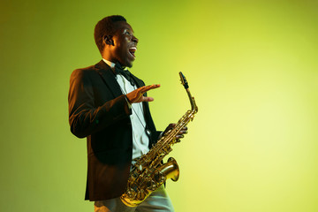 Young african-american jazz musician playing the saxophone on gradient yellow-green studio...