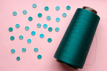 Bobbin with green thread and blue buttons on a pink background close-up, concept of accessories for sewing.