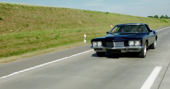 TRACKING Couple traveling together in an old classic vintage 70s muscle car. 4K UHD RAW graded footage