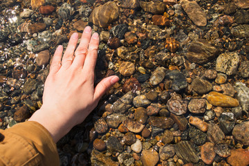 Clear water in the lake on a sunny day. Female hand touches the water.