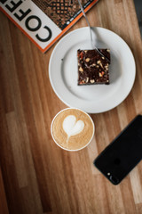 Cappuccino heart coffee on table with brownie and iPhone
