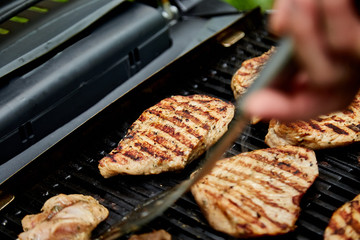 Grilled turkey meat. Hand of young man grilling some meat meat skewers on huge gas grill