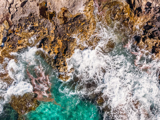 Top view Azure blue sea with waves beating on beach and rocks. Aerial photo.