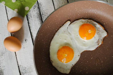 Fried eggs in a pan and raw eggs are on the table