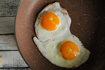 Fried eggs in a pan and raw eggs are on the table