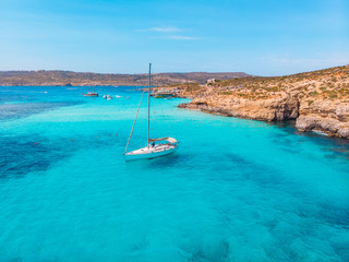 White yacht stands in azure transparent water sea, beach Blue Lagoon Comino Malta. Aerial view