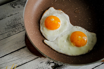 Fried eggs in a pan and raw eggs are on the table