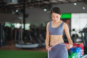 Woman measuring waistline with a white tape measure