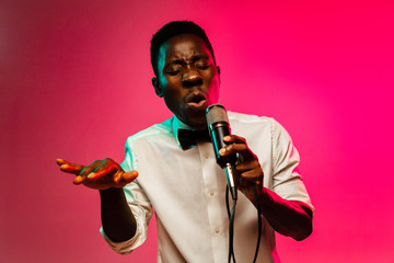 Young african-american jazz musician singing a song on gradient pink-red background in neon light....