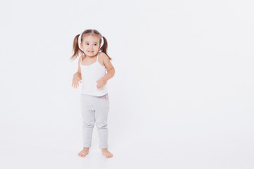 a little girl indulges in a white background: dancing, shy, shows her thumb