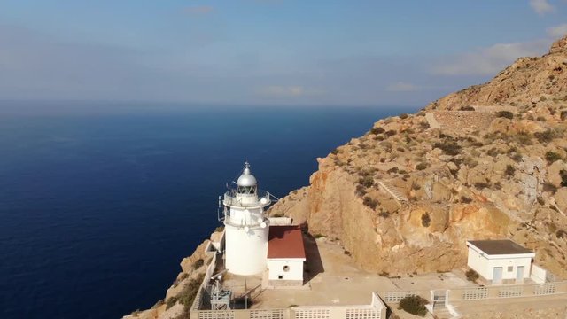 A beautiful white lighthouse stands high on the rocks at Cabo Tinoso near the Spanish port city of Cartagena. The sun is shining and the sea is blue.