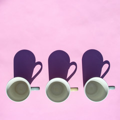 Empty coffee and tea cups stand in row on pink background in sunlight with shadows. Top view, flat lay. Minimal style. Art design.