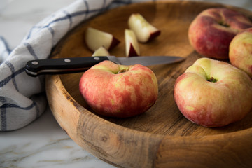 Plattpfirsiche mit Messer und Geschirrtuch in Holz Schale auf Küchen Marmor Tisch